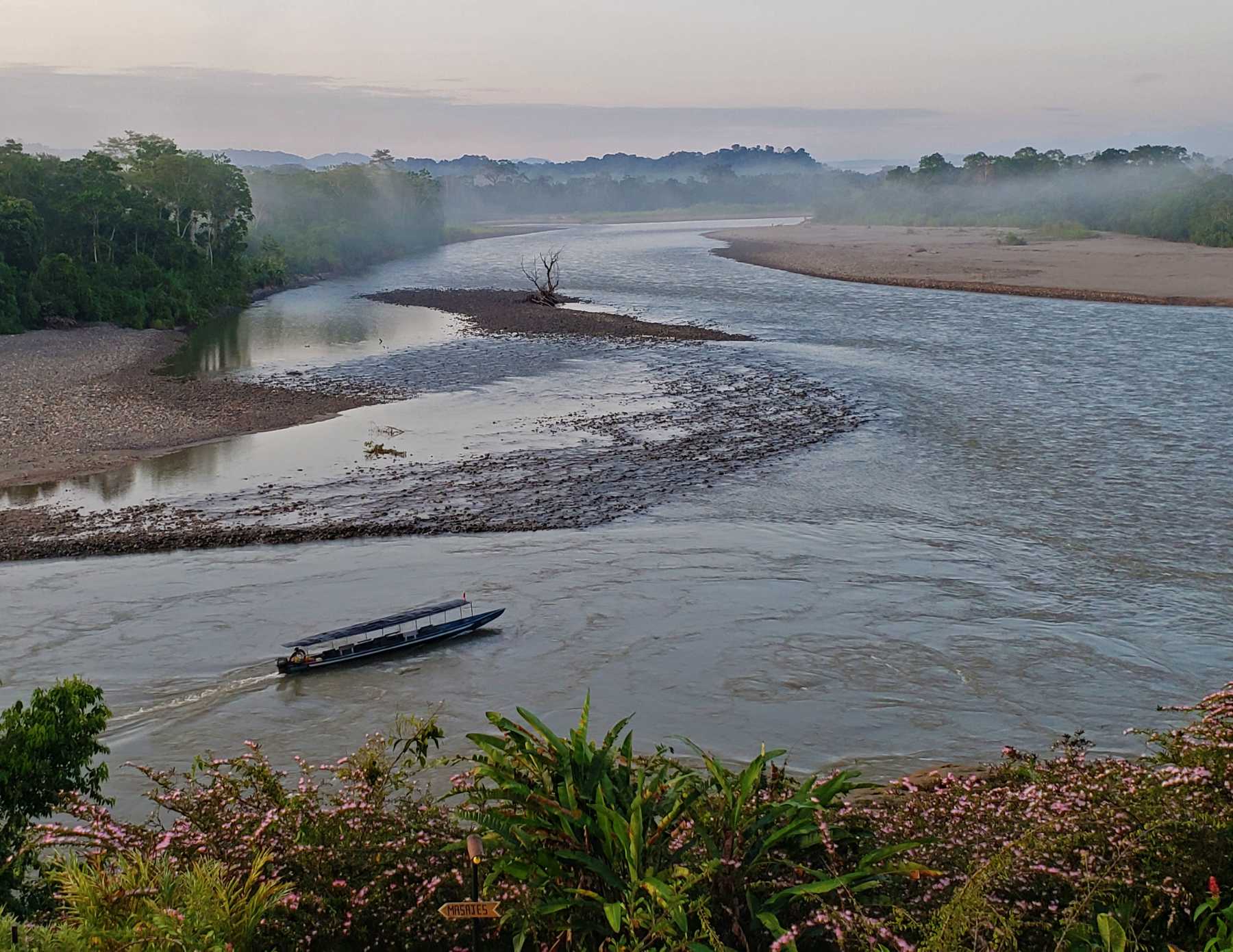 small river boat motoring upstream on jungle river in light morning fog